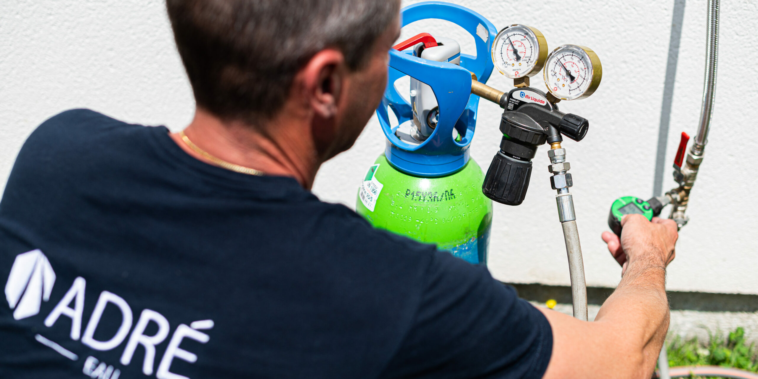 Un technicien inspectant un système de canalisation à l'aide d'une bouteille de gaz équipée de manomètres pour une recherche de fuite.